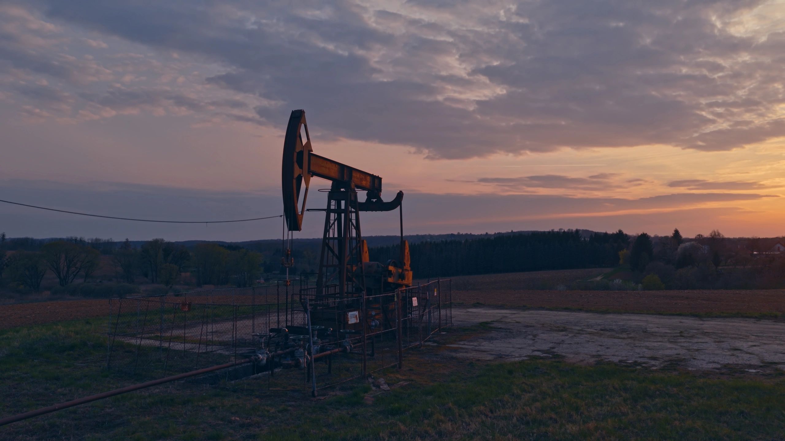 Oil pump jack operating in rural field at sunset